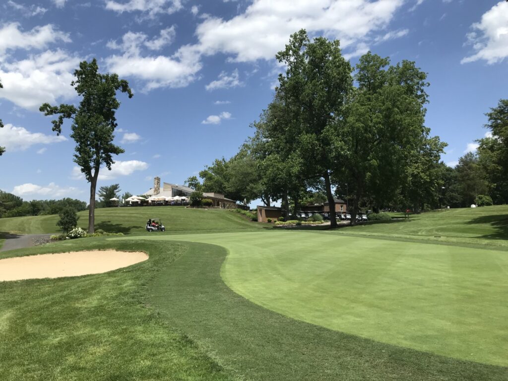 A putting green and a sand trap on a golf course. An angular building stands on a hill in the distance.