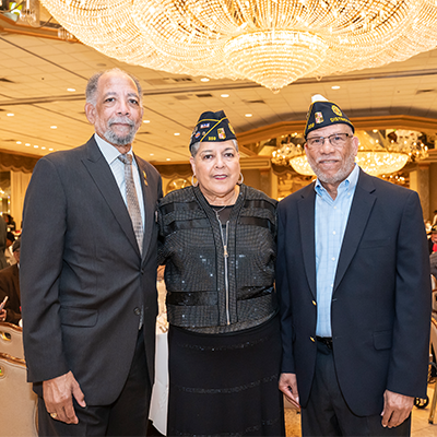 Two men and a woman dressed in suits and a dress standing in a banquet hall at a veterans appreciation event