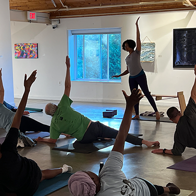 A group of people doing yoga indoors. There is an instructor in the background directing them