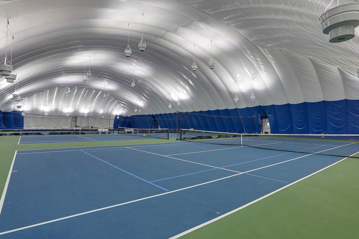 Two tennis courts inside a blue and white tennis bubble with a curved dome ceiling.
