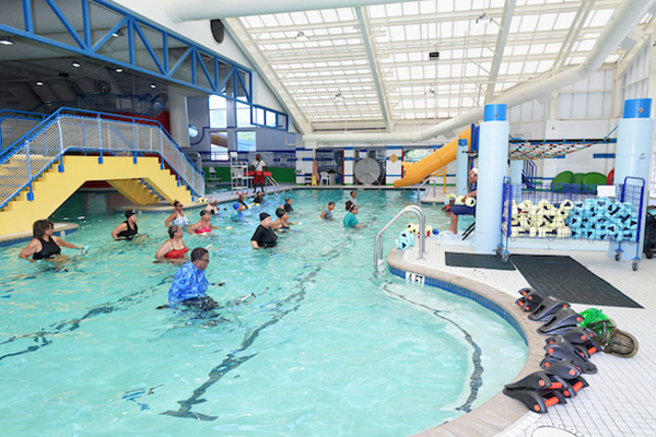 Several dozen people ride special stationary bikes set up in the water of an indoor pool.