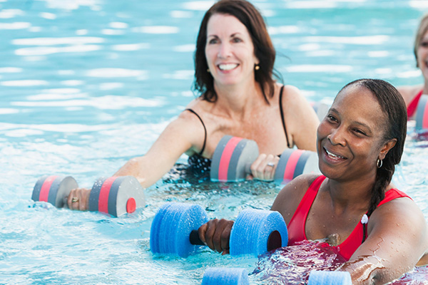 Three smiling women exercise with special water dumbbells in a pool.