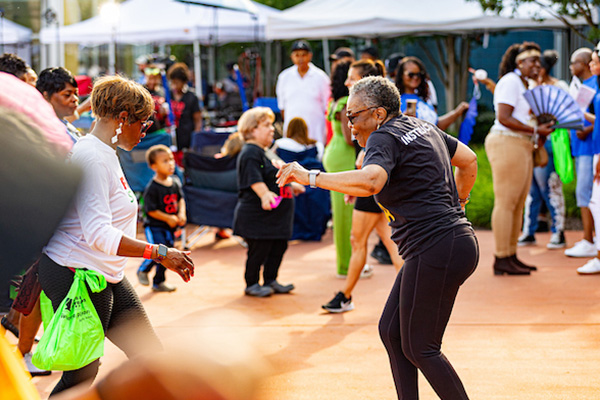 People dance together near a line of vendor tents where other people are gathered.