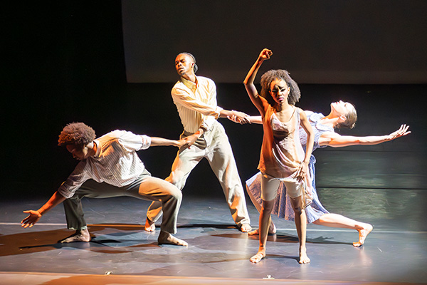 Two men and two women perform modern dance choreography barefoot on a stage.