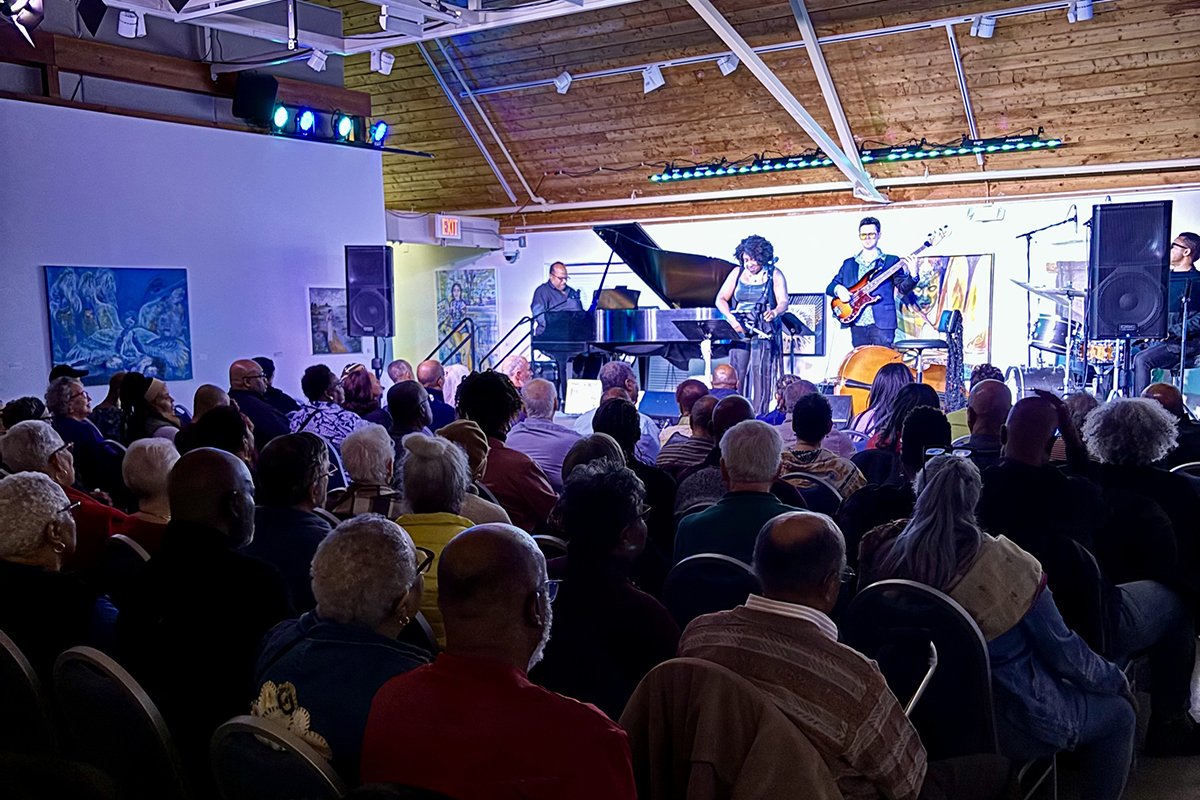 A band performs in front of a seated audience in an art gallery.