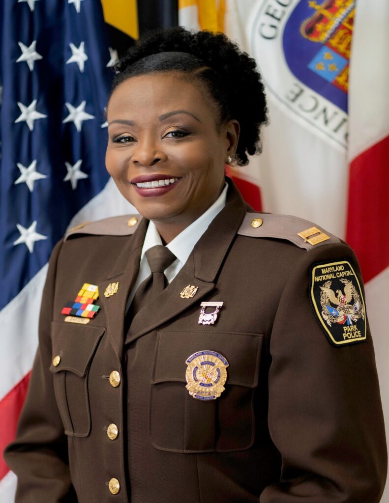 Uniformed park police official in dress uniform, photographed before American, Maryland, and Prince George's County flags.