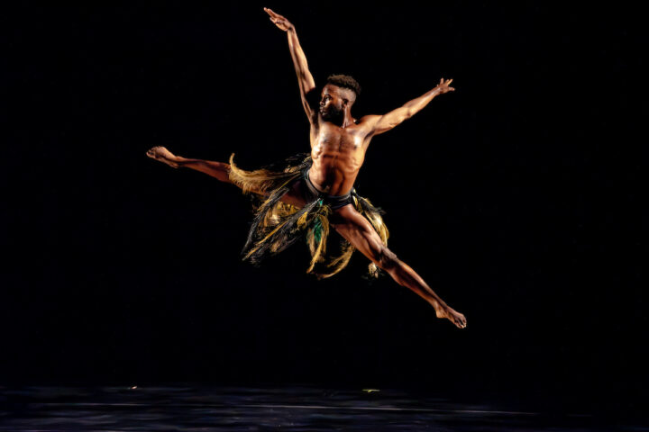 Male dancer in a costume with feathers jumps and dances on stage.