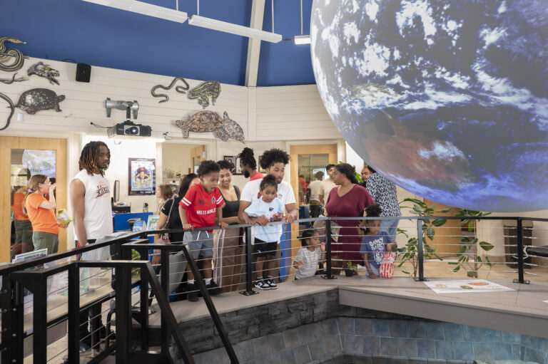 Museum visitors gather around a large suspended globe exhibit, viewing interactive displays and educational exhibits inside a nature center.